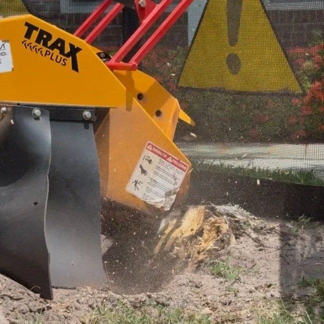 Stump grinding grinding a stump, with a caution sign in the background and flying soil dust.