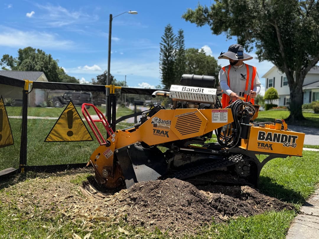 Bandit TRAK outdoor stump grinder in use, worker in safety gear, sunny residential area.