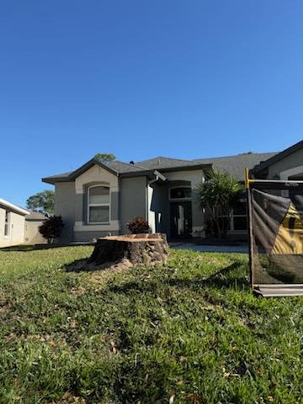 Front view of a house with a tree stump in the yard under a clear blue sky.