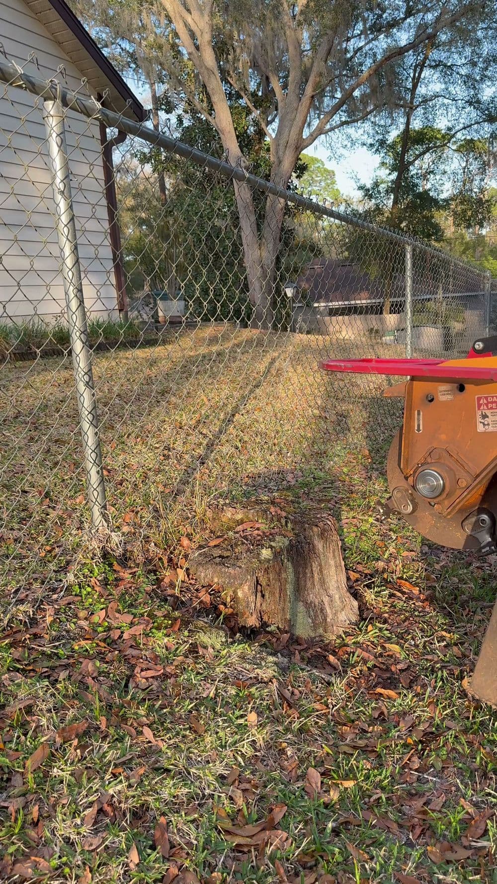 Tree stump next to a chain-link fence and landscaping equipment in a yard.
