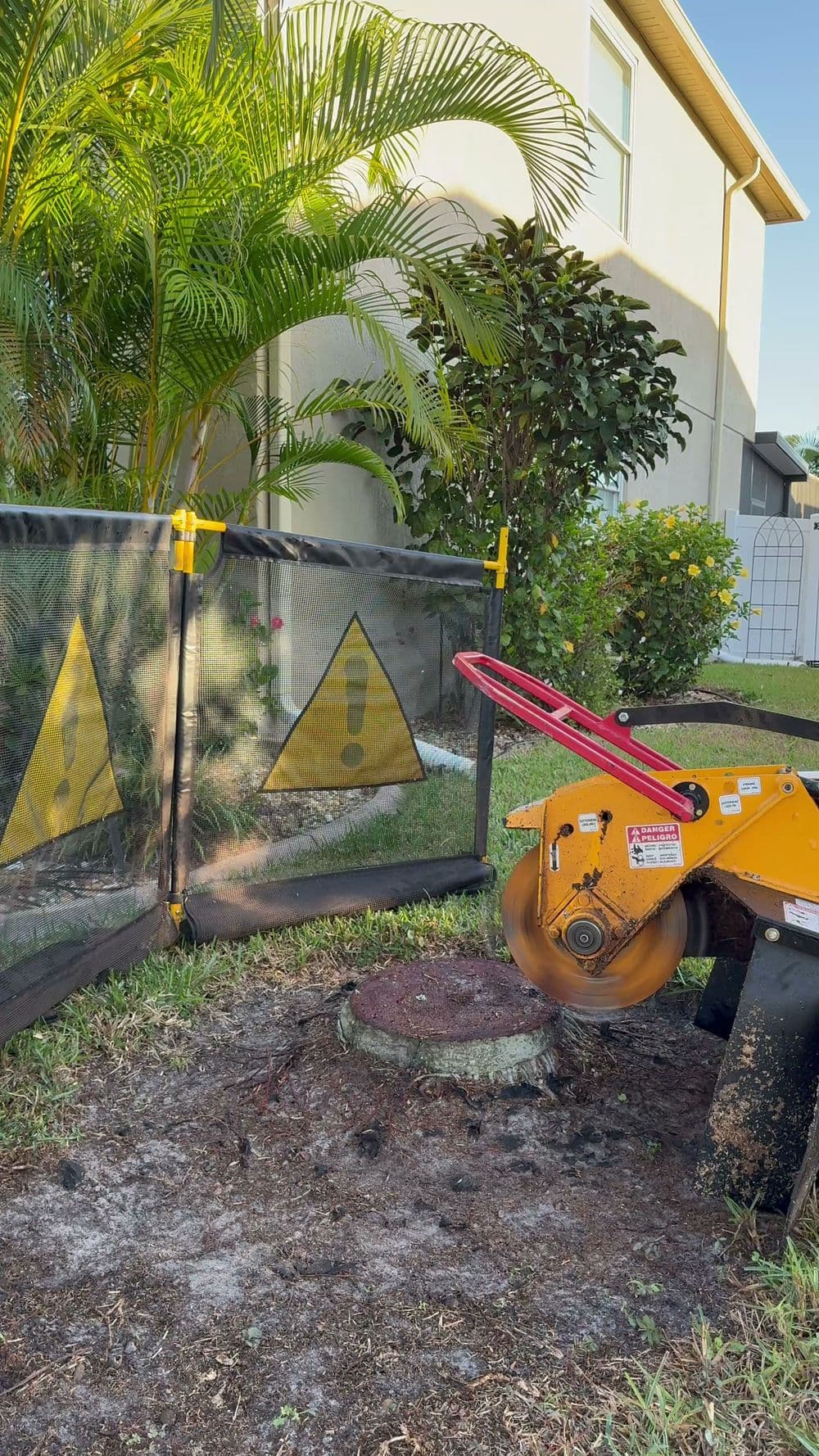 Stump grinder near caution signs in a residential yard surrounded by greenery.