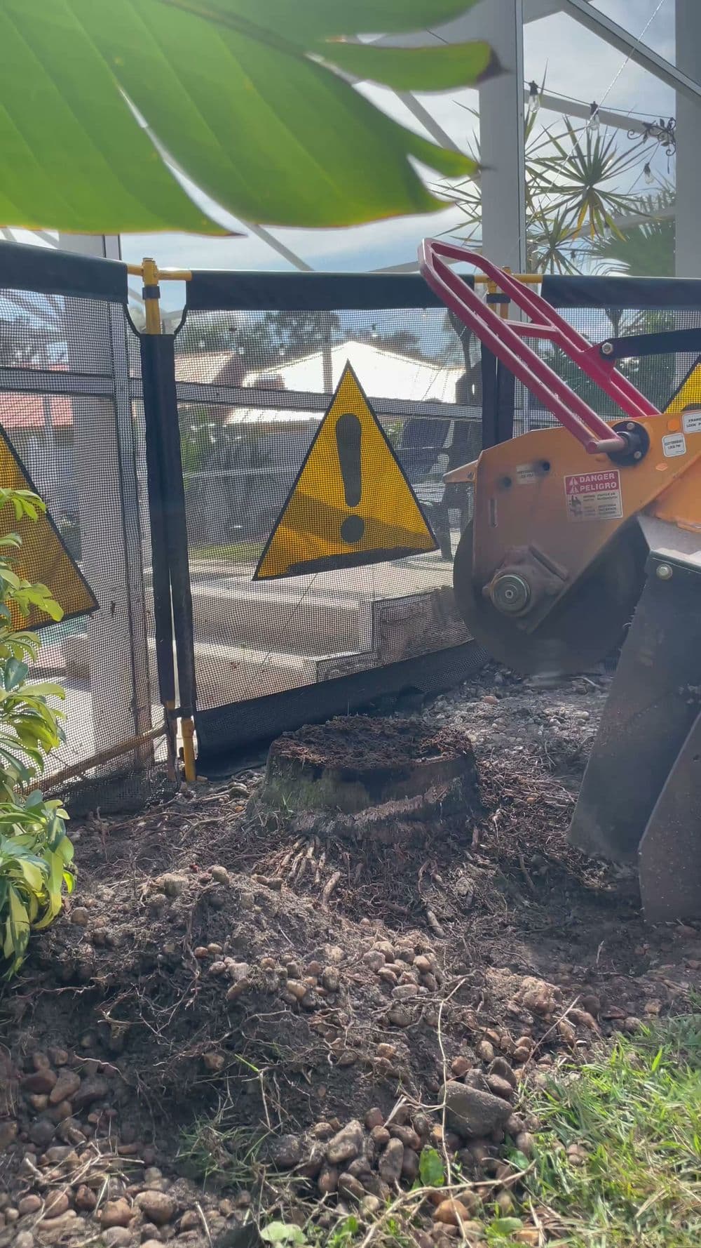 Stump removal equipment near a construction site with warning signs and vegetation.
