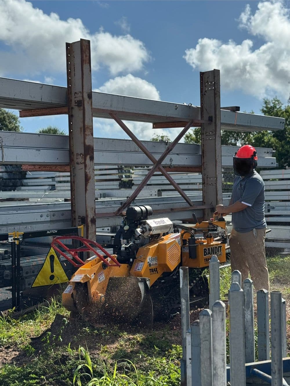 Man operating a Bandit stump grinder on a construction site with metal framework in background.